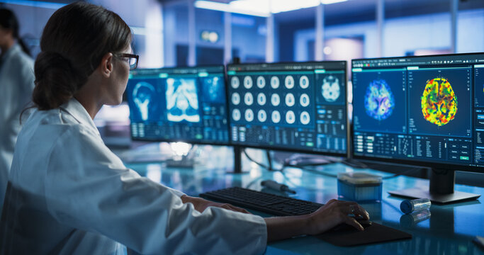 Medical Research Center Laboratory: Caucasian Female Neurologist Using Desktop Computer With MRI And PET Scans Of a Brain. Professional Doctor Looking For Areas of Patient's Brain Damaged By Stroke.