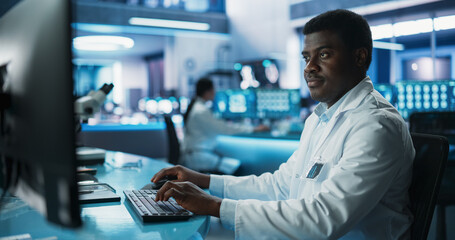 Black Male Doctor Using Desktop Computer In Modern Hospital Medical Research Laboratory. African...