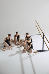 Behind the scenes of ballet. Four elegant teen girls, baller dancers sitting on floor, getting ready for dance, adjusting pointe shoes. Concept of ballet, art, dance studio, classical style, youth