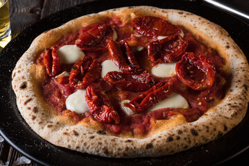 Pizza with mozzarella and sun-dried tomatoes on a black plate. Side view, close up.