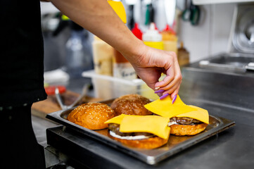 Chef preparing cheeseburgers, placing cheese on patties, showcasing the hands-on aspect of fast food preparation