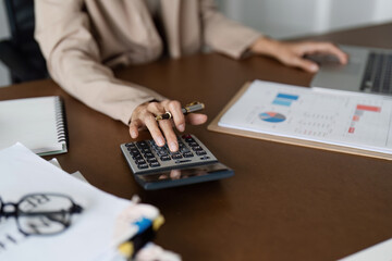 Businesswoman using a calculator to calculate numbers on a company's financial documents, she is...