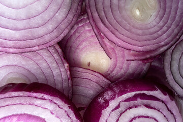 Slices of red onion neatly arranged on a white background. The vibrant purple tones and intricate rings create a visually appealing pattern. The translucence adds depth and texture to the composition.