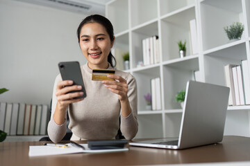 Woman using laptop computer and mobile phone holding credit card for shopping online - obrazy, fototapety, plakaty