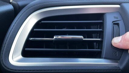 Closeup of a man’s hand opening and adjusting the heating and cooling air vent on a vehicle dashboard.