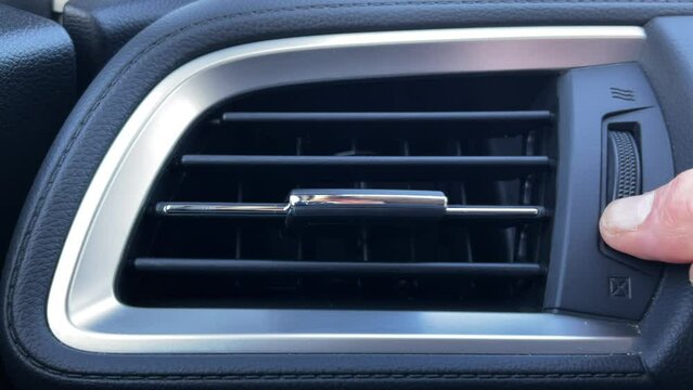 Closeup of a man’s hand opening and adjusting the heating and cooling air vent on a vehicle dashboard.