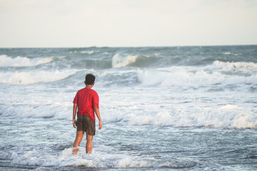 Indonesian young man in red is standing alone at Wavy Beach during the day. Concept for solo...