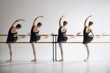 Four teen girls, ballet dancers, training with barre, standing in pose with one leg extended against grey studio background. Concept of ballet, art, dance studio, classical style, youth