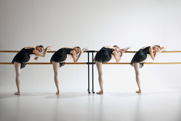 Tenderness in every move. Elegant beautiful teen girls, ballerinas training next to barre, showing flexibility against grey studio background. Ballet, art, dance studio, classical style, youth concept