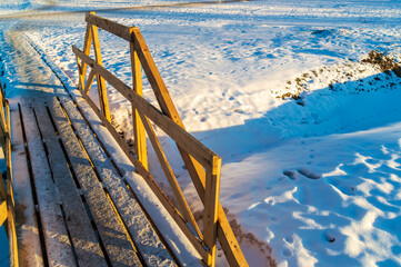 A wooden bridge over a small stream in the snow. The bridge is wooden and has a rustic feel to it....