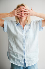 Pretty woman hiding face in her hands. Beautiful female covering face by fingers. Young woman in casual clothes posing on light background.