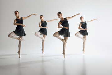 Dance in harmony. Beautiful teen girls, ballerinas in black leotards and pointe in motion, dancing against gray studio background. Concept of ballet, art, dance studio, classical style, youth