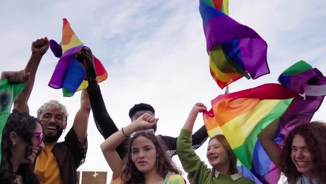 Group of LGBTQIA people celebrating the pride day, dancing raising hands and holding rainbow flags in support of the Homosexual community. Copy space video.