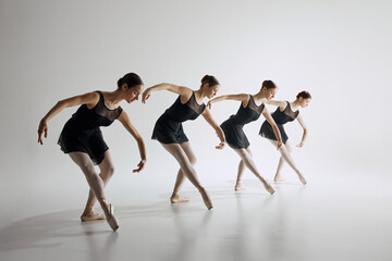 Four young girls, ballet dancers in black leotards training, showing flexibility and synchronized choreography on grey studio background. Concept of ballet art, dance studio, classical style, youth