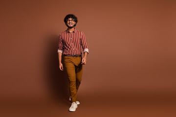 Fototapeta premium Full size photo of nice young man walk empty space wear striped shirt isolated on brown color background