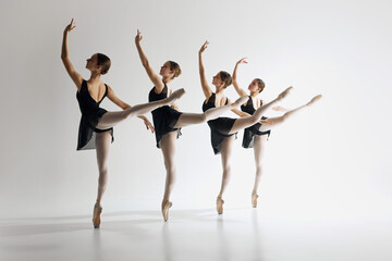 Graceful ballet performance. Four graceful ballet dancers, teens in black leotards and pointe standing in md-pose, practicing against grey studio background. Concept of ballet art, dance studio, youth