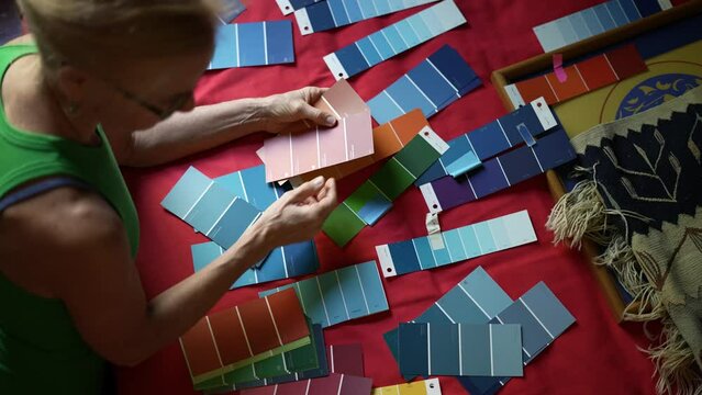 Overhead view of mature blonde woman choosing mixing and matching swatch colors for paint in her home.