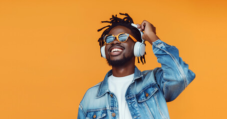 Portrait of happy modern african young man listening to music with headphones on orange background