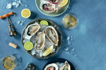 Oysters on ice, with various toppings and white wine, overhead flat lay shot on a blue slate...