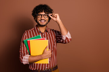 Portrait of nice young man touch eyeglasses book empty space wear striped shirt isolated on brown...