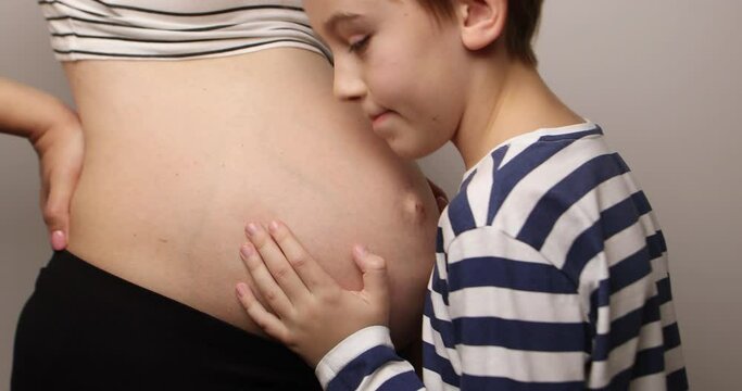 Little boy looking at her mother pregnant tummy. Pregnant mother and son spending time together at home. Pregnancy, family, parenthood, preparation and expectation concepts.