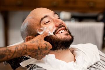 Fototapeta premium Customer getting a beard trim in a barber shop, small business