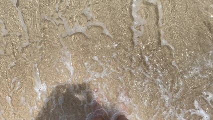 a person feet photo on beach sand with the ocean water splashing up.