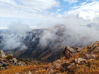 Clouds swirling around rocky mountain peaks with golden grass in the foreground