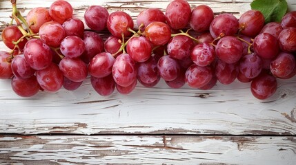   A red cluster of grapes atop a white wooden table, adorned by a green leaf