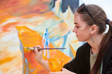 Attractive female painter passionately draws picture with paintbrush for outdoor street exhibition,...