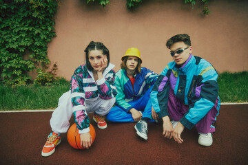 Retro street style. 90s inspired fashion. Young people, friends wearing colorful tracksuits, sunglasses, shoes and accessories, sitting outdoor. Concept of 90s, fashion, youth culture, old-style trend