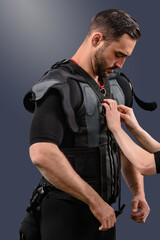 Personal trainer fastening EMS suit on young sporty man, Fitness innovation: Male model with electro muscle stimulator, perfect for showcasing exercise technology - obrazy, fototapety, plakaty