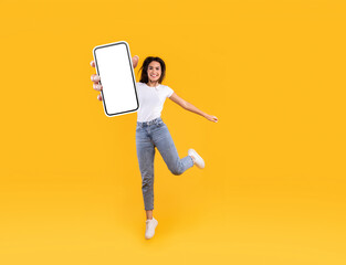 Happy woman showing white empty smartphone screen and jumping