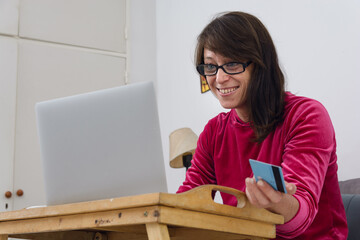 Latina adult woman at home using laptop making online purchases with her credit card