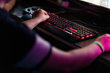 Close-up of keyboard and teenager playing video game on desktop PC in glow blue light