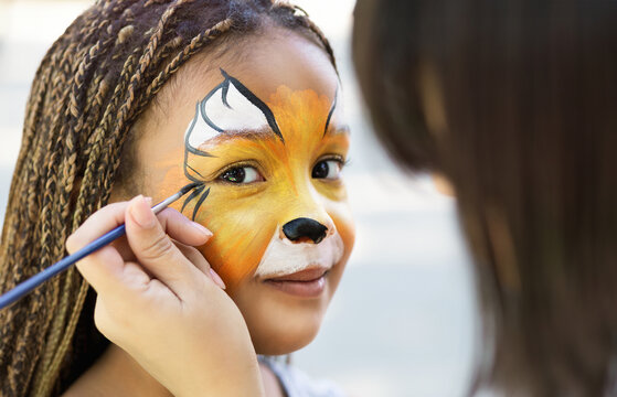Little girl getting her face painted by face painting artist.