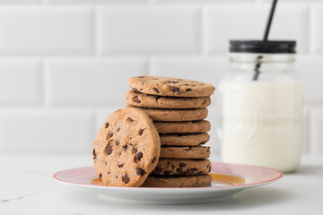 Cookies are spread out on a plate, a glass of fresh milk. Homemade cookies with chocolate chips. - obrazy, fototapety, plakaty