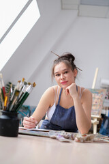 Young female artist paints a picture with oil on canvas in art studio