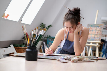 Young female artist paints a picture with oil on canvas in art studio