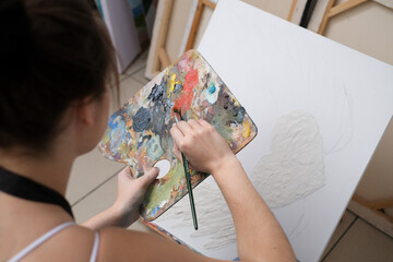 Young female artist paints a picture with oil on canvas in art studio
