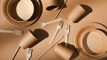 A set of paper utensils and wooden cutlery on a brown background. Eco friendly, zero waste concept, web banner. Top view