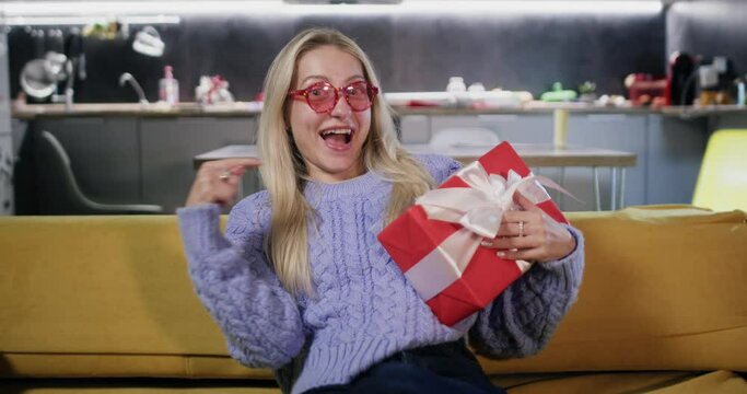Young lady dressed in sweater skillfully catches box wrapped in holiday paper. Woman pleasantly taken aback by gift delivered from online marketplace