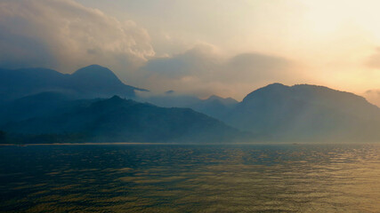 Morning fog over the island in the rays of dawn. View from the sea to a tropical island at dawn and...