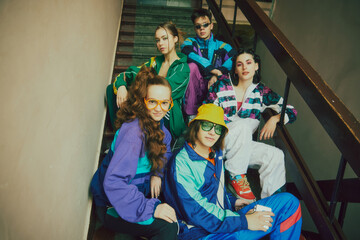 Vibrant youth atmosphere. Young boys and girls, friends wearing colorful 90s style sportswear, posing on stairs, entryway. Concept of 90s, fashion, youth culture, old-style trends