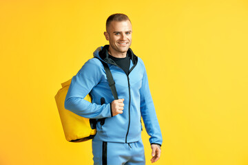 Smiling sporty man in sports suit  and back pack over yellow background