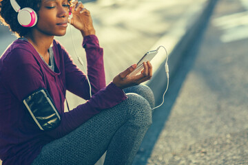 Active young woman resting and listening to music with headphones outdoors