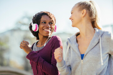 Two women jogging together with headphones in an urban park