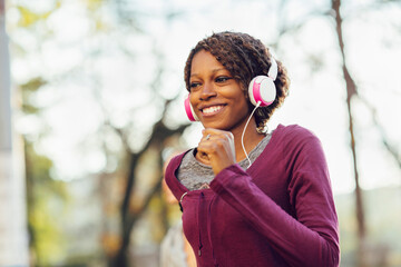 Smiling young active woman jogging outdoors with headphones on
