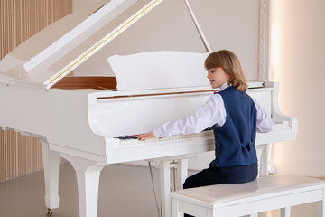 A little boy plays a big white piano in a bright sunny room