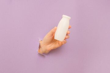White bottle of probiotic yogurt for digestive system in hand with lilac background. Dietary...